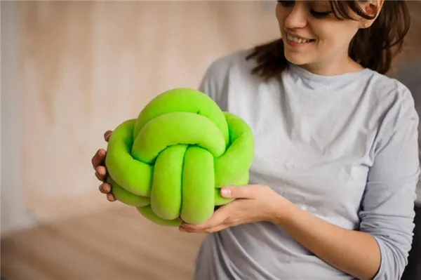 Девушка улыбается и смотрит на зеленую подушку-узел в своих руках