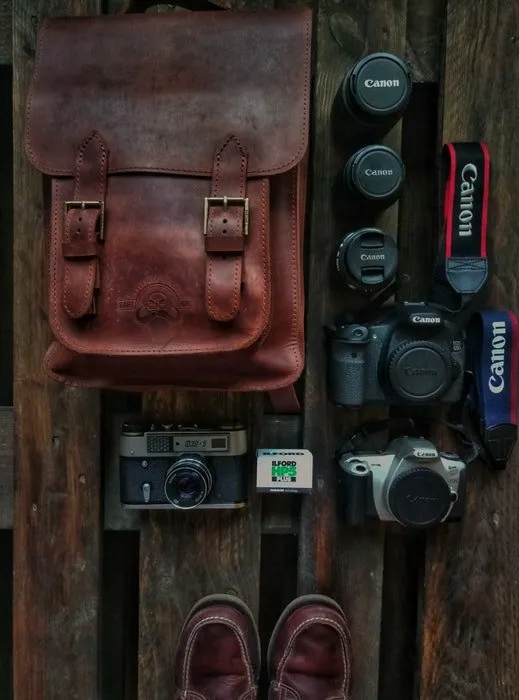верхний снимок кожаной сумки для камеры и оборудования, разложенного на деревянной поверхности